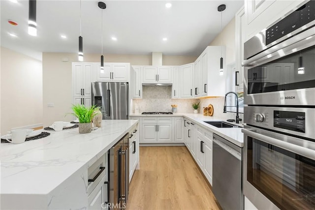 kitchen featuring stainless steel appliances, a sink, white cabinetry, light wood-type flooring, and tasteful backsplash