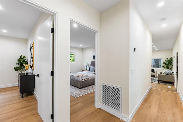 hall featuring light wood finished floors, baseboards, visible vents, and recessed lighting