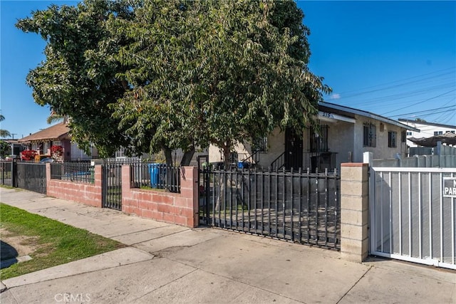 view of property hidden behind natural elements featuring a fenced front yard, a gate, stucco siding, and central AC unit