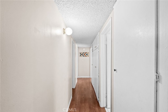 corridor with a textured ceiling, wood finished floors, and baseboards