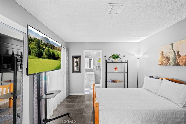 bedroom with a textured ceiling, ensuite bathroom, visible vents, and baseboards