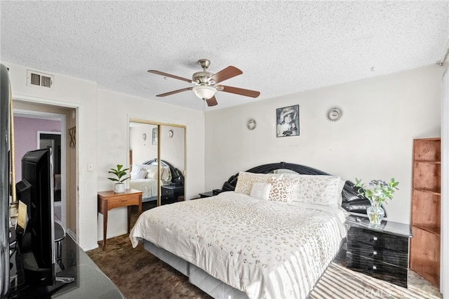 bedroom with a textured ceiling, visible vents, a ceiling fan, a closet, and dark carpet