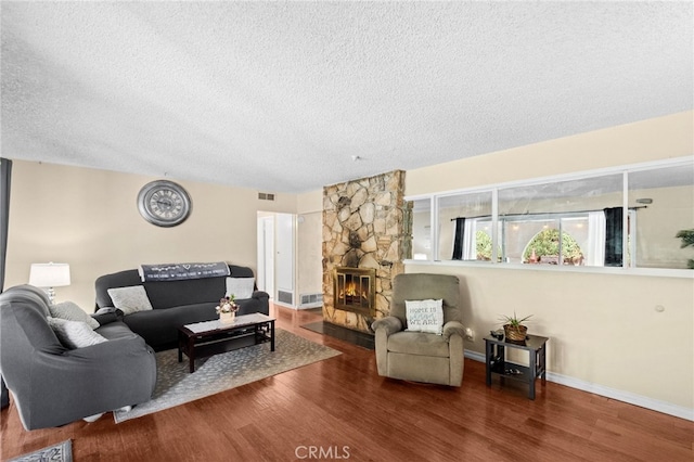 living area featuring visible vents, a stone fireplace, a textured ceiling, and wood finished floors