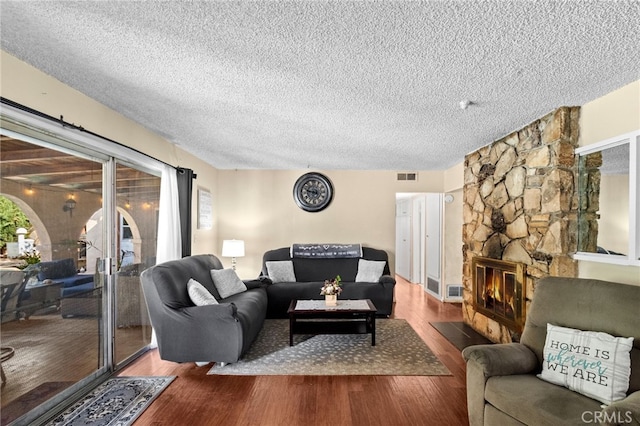 living room with a textured ceiling, a fireplace, wood finished floors, and visible vents