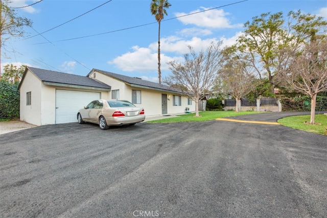 ranch-style home with an attached garage, fence, aphalt driveway, and stucco siding