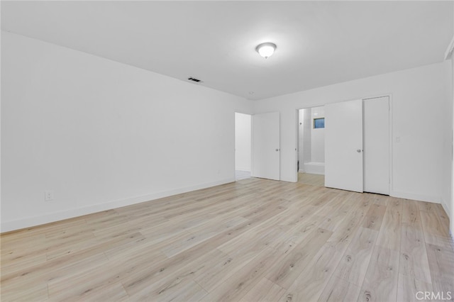 spare room featuring light wood-type flooring, visible vents, and baseboards