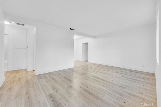 empty room featuring light wood finished floors, baseboards, and visible vents