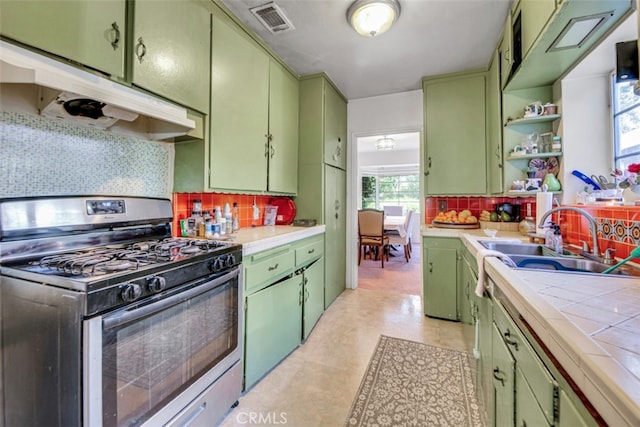 kitchen with tile countertops, under cabinet range hood, green cabinets, a sink, and gas stove