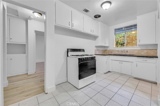 kitchen with light tile patterned floors, white gas stove, a sink, visible vents, and dark countertops