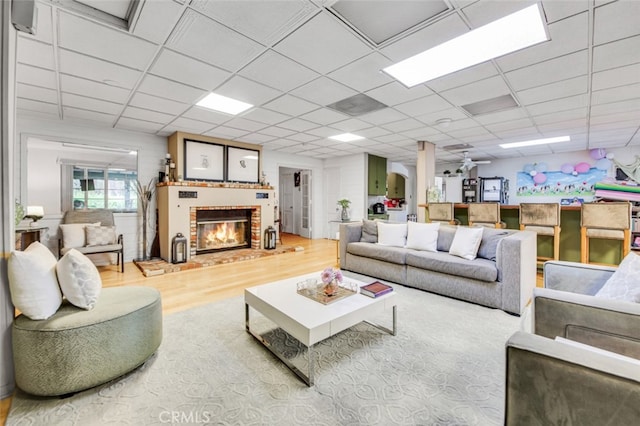 living area with a paneled ceiling, a brick fireplace, and wood finished floors