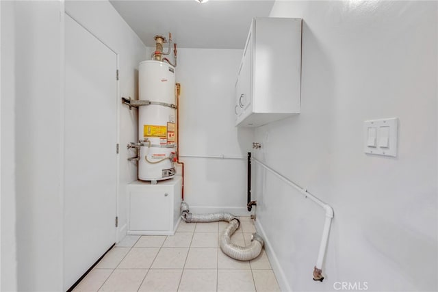 washroom with light tile patterned floors, secured water heater, baseboards, and cabinet space