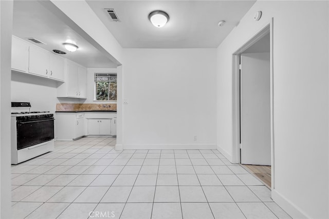 kitchen with white gas stove, light tile patterned flooring, visible vents, baseboards, and white cabinets