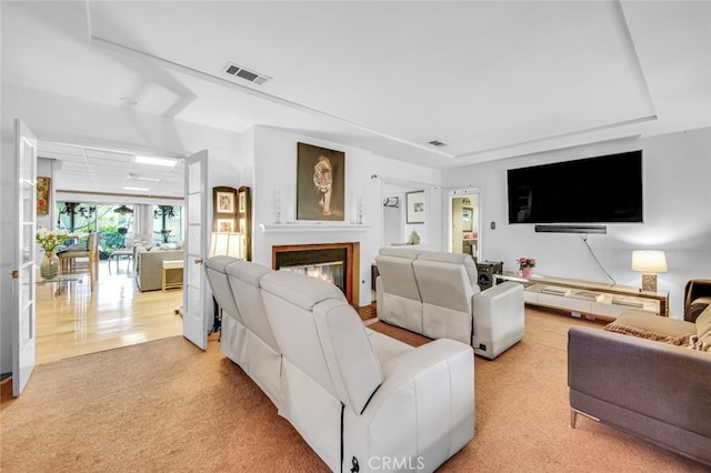 living area with light carpet, a glass covered fireplace, and visible vents