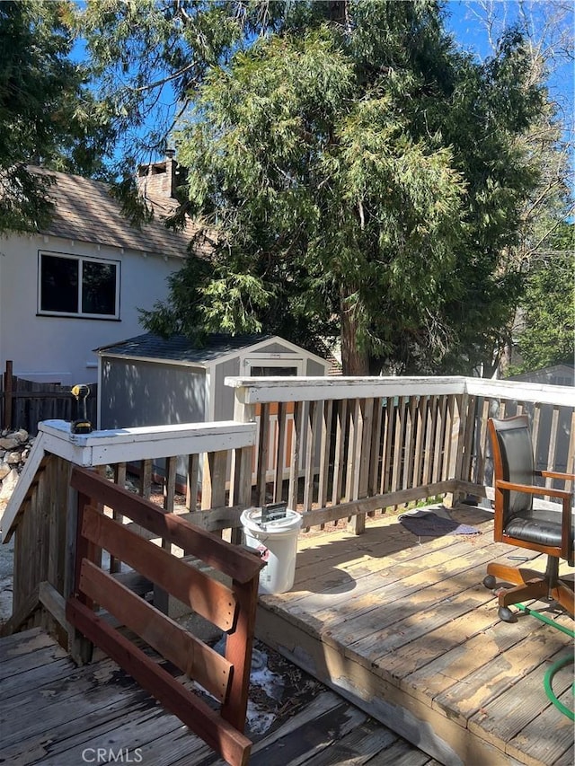 wooden terrace featuring an outbuilding, fence, and a shed