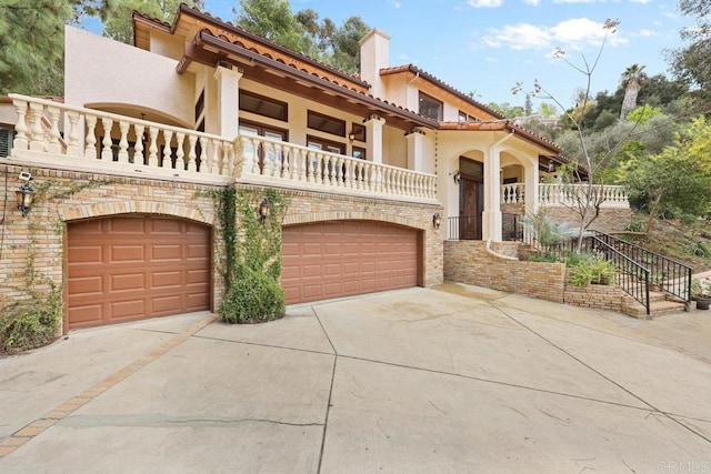 mediterranean / spanish home featuring a chimney, stucco siding, a balcony, a garage, and driveway