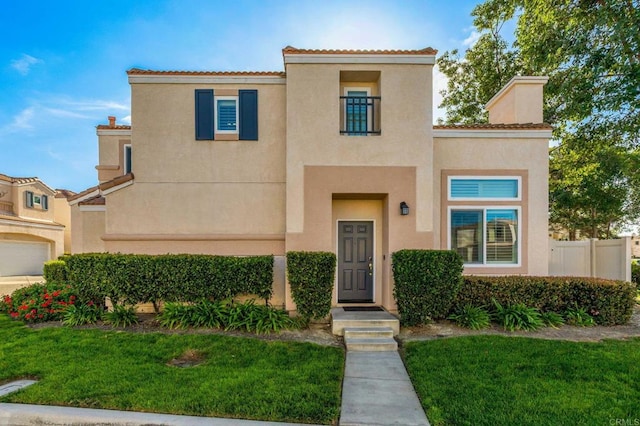 mediterranean / spanish-style home featuring fence, a front lawn, and stucco siding