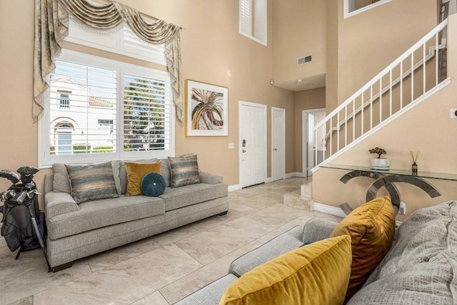 living area featuring stairway, marble finish floor, a towering ceiling, baseboards, and visible vents