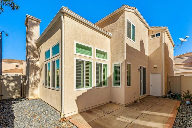 rear view of house with fence, stucco siding, and a patio