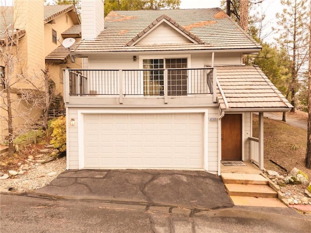 view of front of home with aphalt driveway, a balcony, a garage, a tiled roof, and a chimney