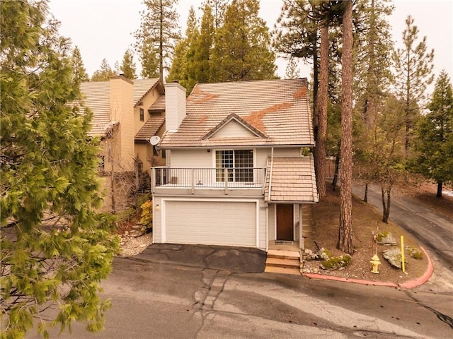 view of front of property featuring driveway, a balcony, a chimney, a tiled roof, and an attached garage