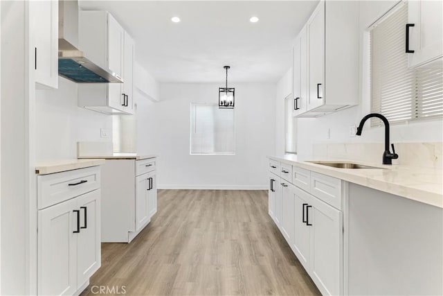 kitchen featuring recessed lighting, a sink, white cabinets, wall chimney range hood, and light wood-type flooring