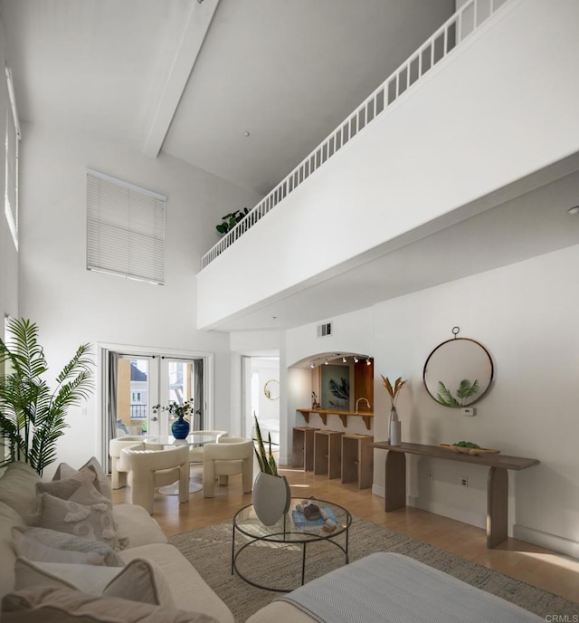 living area featuring a high ceiling, wood finished floors, visible vents, french doors, and beamed ceiling