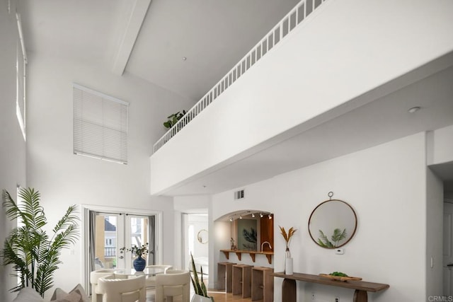 living room featuring arched walkways, visible vents, a towering ceiling, french doors, and beam ceiling