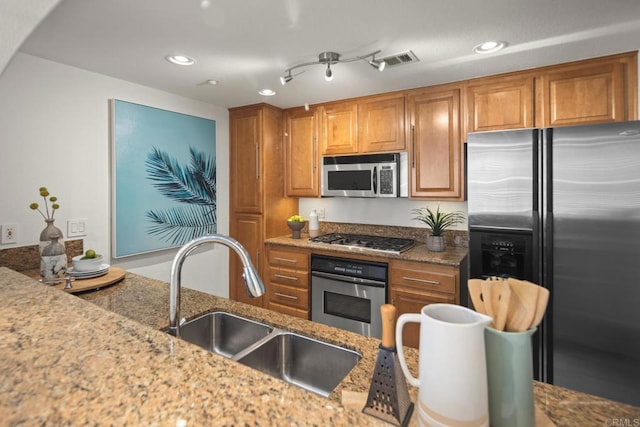 kitchen with stainless steel appliances, brown cabinetry, visible vents, and a sink