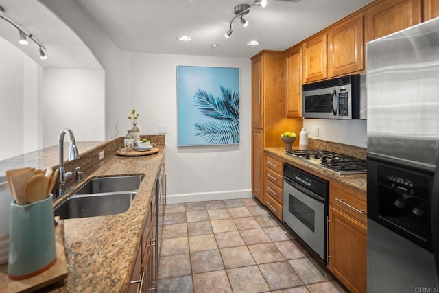 kitchen featuring a sink, baseboards, appliances with stainless steel finishes, light stone countertops, and brown cabinetry