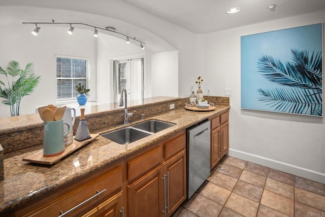 kitchen featuring stainless steel dishwasher, brown cabinetry, a sink, and light stone countertops