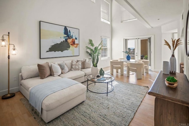 living room featuring french doors, wood finished floors, a towering ceiling, and baseboards