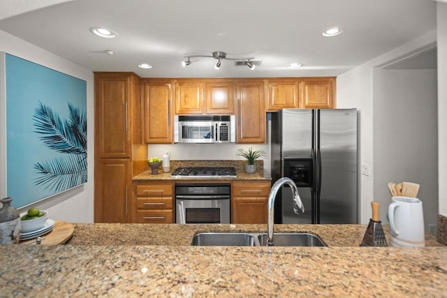 kitchen featuring stainless steel appliances, light stone counters, a sink, and brown cabinets