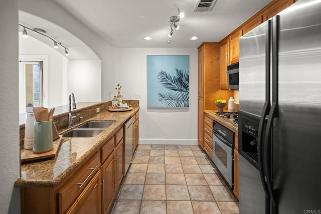 kitchen with stone counters, a sink, visible vents, appliances with stainless steel finishes, and brown cabinetry