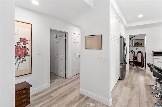 hallway with light wood-type flooring, baseboards, and recessed lighting