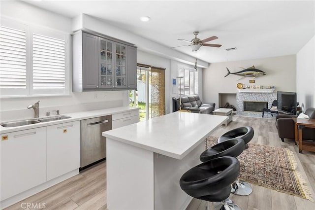 kitchen featuring a sink, a kitchen breakfast bar, stainless steel dishwasher, gray cabinets, and glass insert cabinets