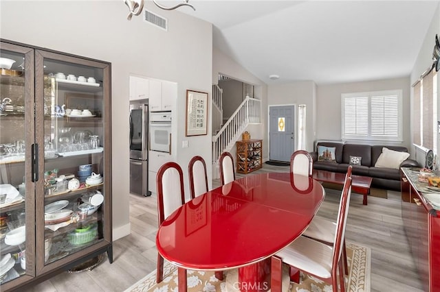 dining area with light wood-style floors, lofted ceiling, visible vents, and stairway