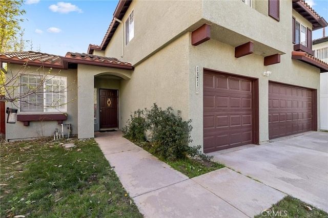 view of exterior entry featuring driveway, a tiled roof, an attached garage, and stucco siding