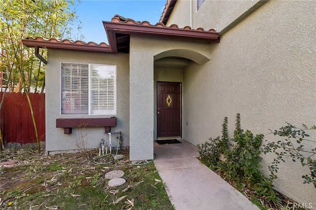 property entrance with fence, a tiled roof, and stucco siding