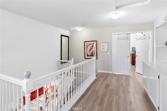 corridor with light wood finished floors, an upstairs landing, and baseboards