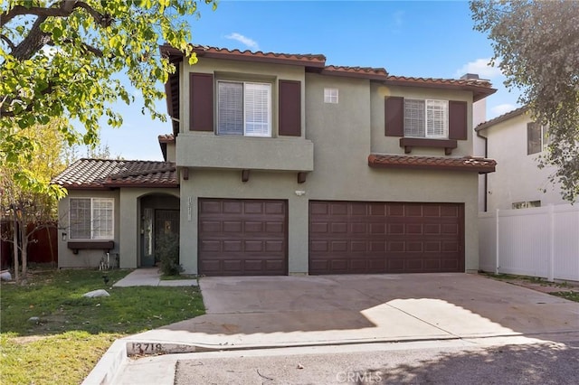 mediterranean / spanish house featuring an attached garage, fence, driveway, stucco siding, and a front yard