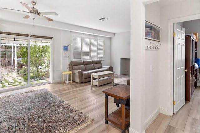 living area featuring a wealth of natural light, light wood-style flooring, visible vents, and a ceiling fan