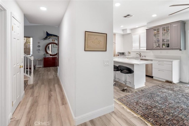 hall with visible vents, a sink, light wood-style flooring, and baseboards