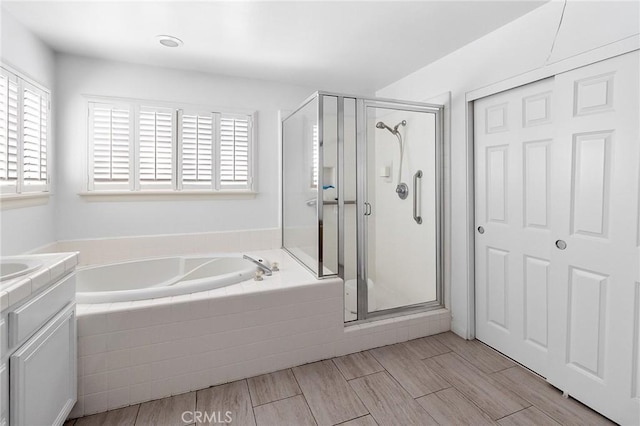 bathroom with a shower stall, vanity, a bath, and wood finish floors