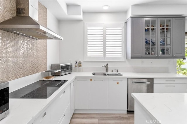 kitchen with dishwasher, wall chimney exhaust hood, black electric cooktop, gray cabinets, and a sink