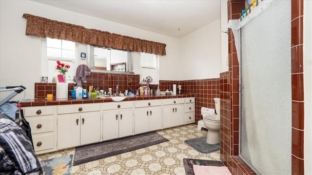 full bathroom with toilet, a wainscoted wall, an enclosed shower, vanity, and tile walls