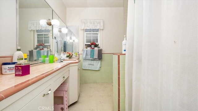 full bathroom featuring curtained shower, wainscoting, tile walls, and vanity