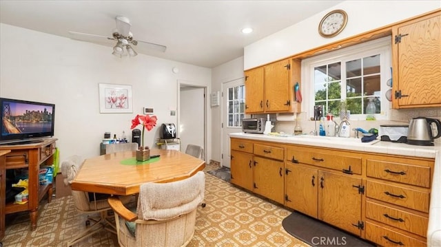 kitchen featuring a ceiling fan, brown cabinets, a sink, and light floors