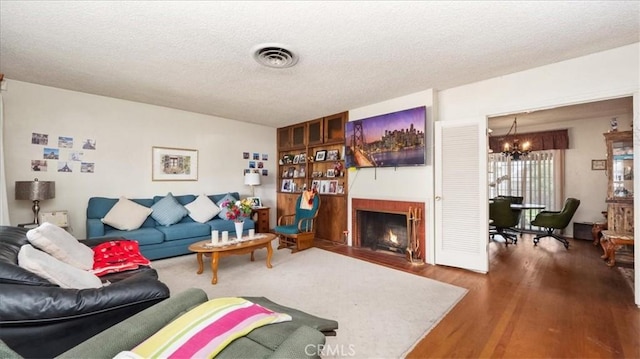 living area featuring visible vents, a fireplace with flush hearth, a textured ceiling, wood finished floors, and a chandelier