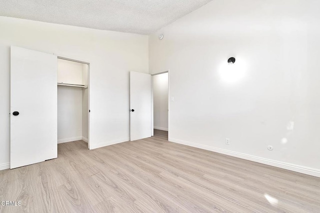 unfurnished bedroom featuring lofted ceiling, a closet, a textured ceiling, light wood-type flooring, and baseboards