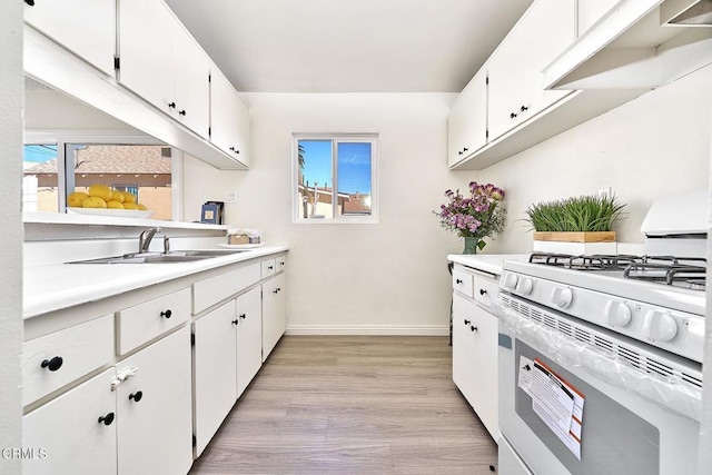 kitchen featuring a sink, white cabinets, light countertops, light wood-type flooring, and white gas range